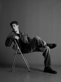 a young man sitting in a chair with his legs crossed and one foot on the ground