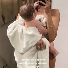 a woman taking a selfie with her baby wrapped in a towel and looking at her phone