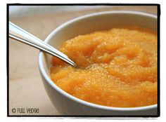 a white bowl filled with orange custard on top of a wooden table next to a spoon