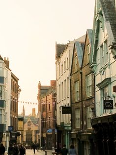 people are walking down the street in an old town with tall buildings on either side