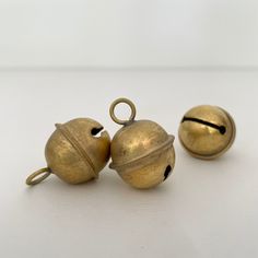 three brass bells sitting on top of a white table next to an open bell with two holes in the middle