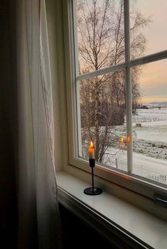 a candle is sitting on a window sill in front of the snow covered field