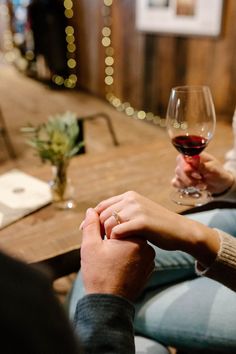 two people holding hands while sitting at a table with wine glasses in front of them