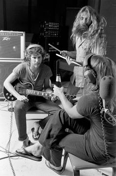 three people are sitting on a chair with guitars and headphones in front of them