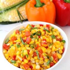 a white bowl filled with corn next to two peppers and an ear of corn on the cob