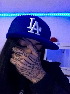 a person wearing a los angeles baseball cap covering their face with both hands and covering his mouth