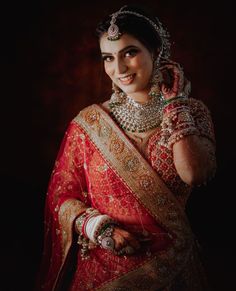 a woman in a red and gold sari with her hands on her head, smiling