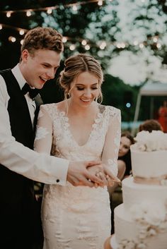 a bride and groom are cutting their wedding cake at an outdoor reception with string lights in the background