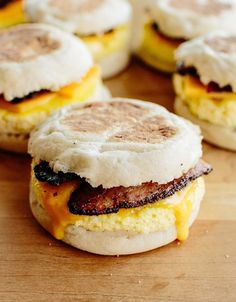 eggs, bacon and cheese on english muffins sitting on a cutting board together