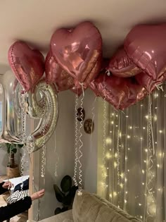 some pink heart shaped balloons hanging from the ceiling in a living room with string lights