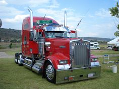 a red semi truck parked on top of a lush green field