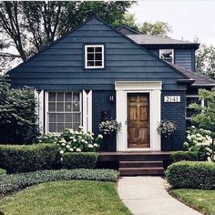 a blue house with white trim and flowers on the front door is surrounded by hedges