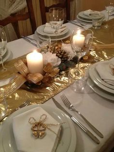 the table is set with white plates and silverware, gold napkins and candles