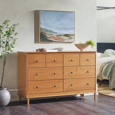 a bedroom with a bed, dresser and painting on the wall next to potted plant