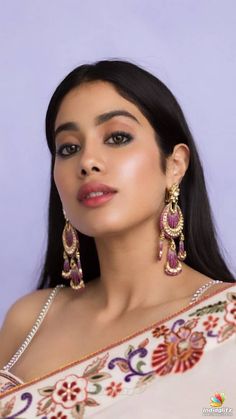 a woman with long black hair wearing large earrings and a white top is posing for the camera