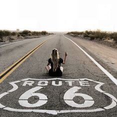 a woman sitting on the side of an empty road with route 66 painted on it