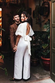 a man and woman standing next to each other in front of a doorway with plants