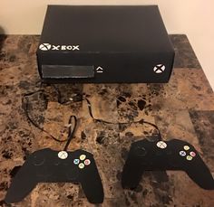 two video game controllers sitting on top of a counter next to a black box with buttons