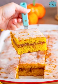 a person is holding a piece of cake with frosting on it and there are oranges in the background