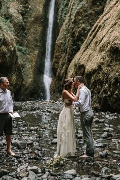 a bride and groom standing in front of a waterfall during their elopetion ceremony