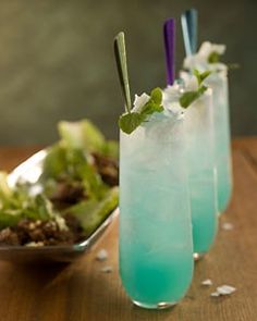 three glasses filled with blue liquid sitting on top of a table next to a salad