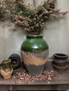 a green vase sitting on top of a wooden table next to other pots and containers