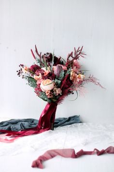 a bouquet of flowers sitting on top of a white bed next to a red ribbon