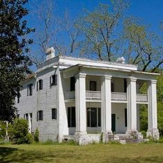 an old white house with columns and pillars in front of it, surrounded by trees