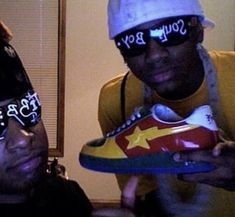 two men wearing sunglasses and hats are holding up shoes with the word soul boy on them