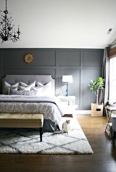 a bedroom with gray walls, white bedding and a dog sitting on the rug