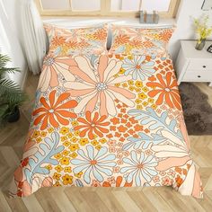 an orange and blue flowered comforter on a wooden floor next to a window