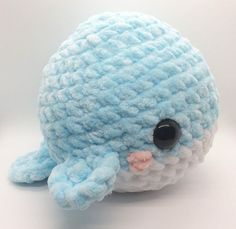 a blue and white stuffed animal on a white surface with one eye open, the other half closed