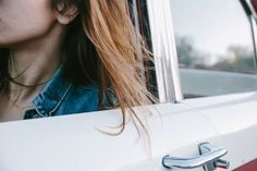 a woman with red hair is looking out the window of a white car and has her hand on the door handle