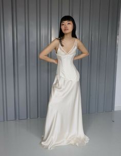 a woman standing in front of a metal wall wearing a white dress and holding her hands on her hips