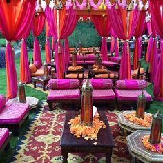 an outdoor wedding setup with pink and orange drapes on the ceiling, couches in the grass