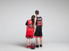 two people standing next to each other in front of a gray background wearing basketball uniforms