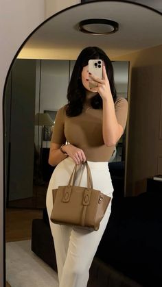 a woman taking a selfie in front of a mirror holding a brown handbag