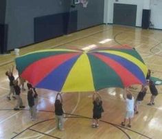 a group of people standing on top of a basketball court holding up a large umbrella