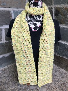 a woman wearing a yellow knitted scarf with multicolored dots on it, standing in front of a brick wall