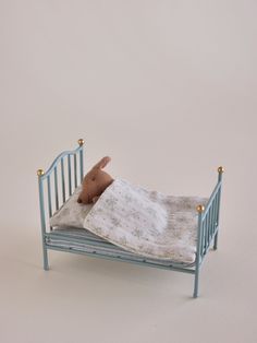 a small toy bed with a stuffed animal on it's side, against a white background