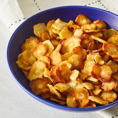 a blue bowl filled with fried potatoes on top of a white table cloth next to a fork