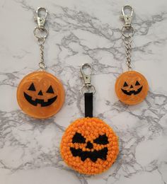 three crocheted pumpkin keychains on a marble surface with two jack - o'- lantern faces