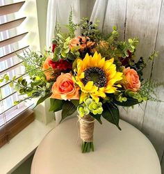 a bouquet of sunflowers and roses sits on a table in front of a window