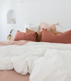 a bed with white sheets and pink pillows on top of it next to a plant