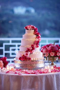 a three tiered wedding cake with pink flowers and candles on a table in front of a balcony