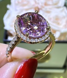 a close up of a person's hand holding a ring with a pink stone