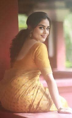 a woman sitting on top of a window sill wearing a yellow dress and smiling