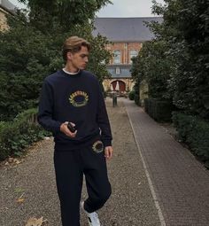 a young man is walking down the street wearing sweatpants and a sweatshirt with an embellishment on it