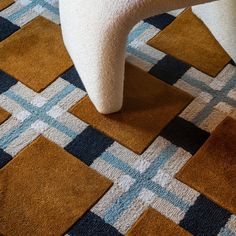 a white chair sitting on top of a patch of carpet next to a rug covered in brown and blue squares