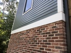 the corner of a brick building with a window on it's side and trees in the background